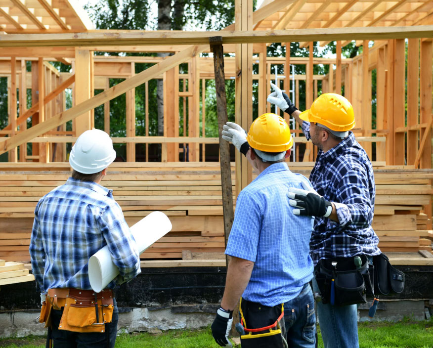 Three construction workers in hard hats review a wooden framing on a building site in progress.