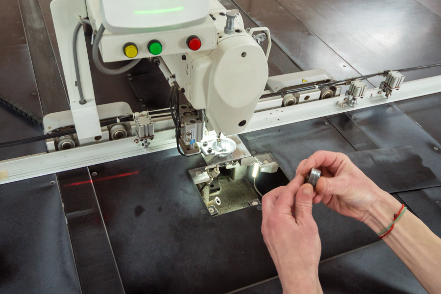 Worker hand-fitting a component into an automated stitching machine on a manufacturing production line